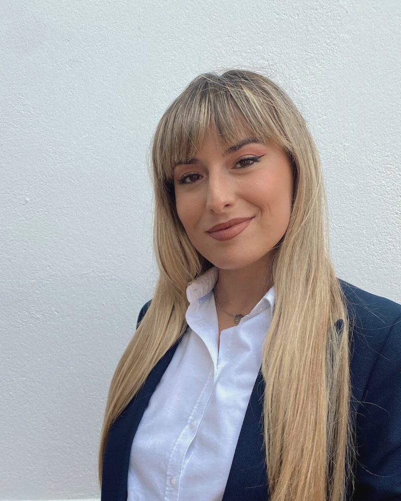 Áurea Fernández, con americana azul marino y camisa blanca, sonríe ante una pared encalada