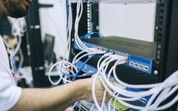 A technician plugging patch cables into a network cabinet with tidy cabling