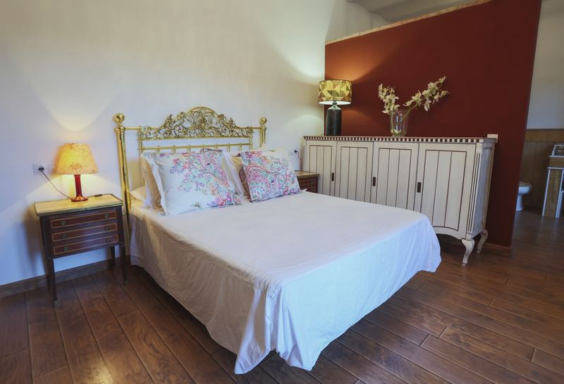 Dormitorio con cama de matrimonio, cabecero de forja dorada y una pared en almagre