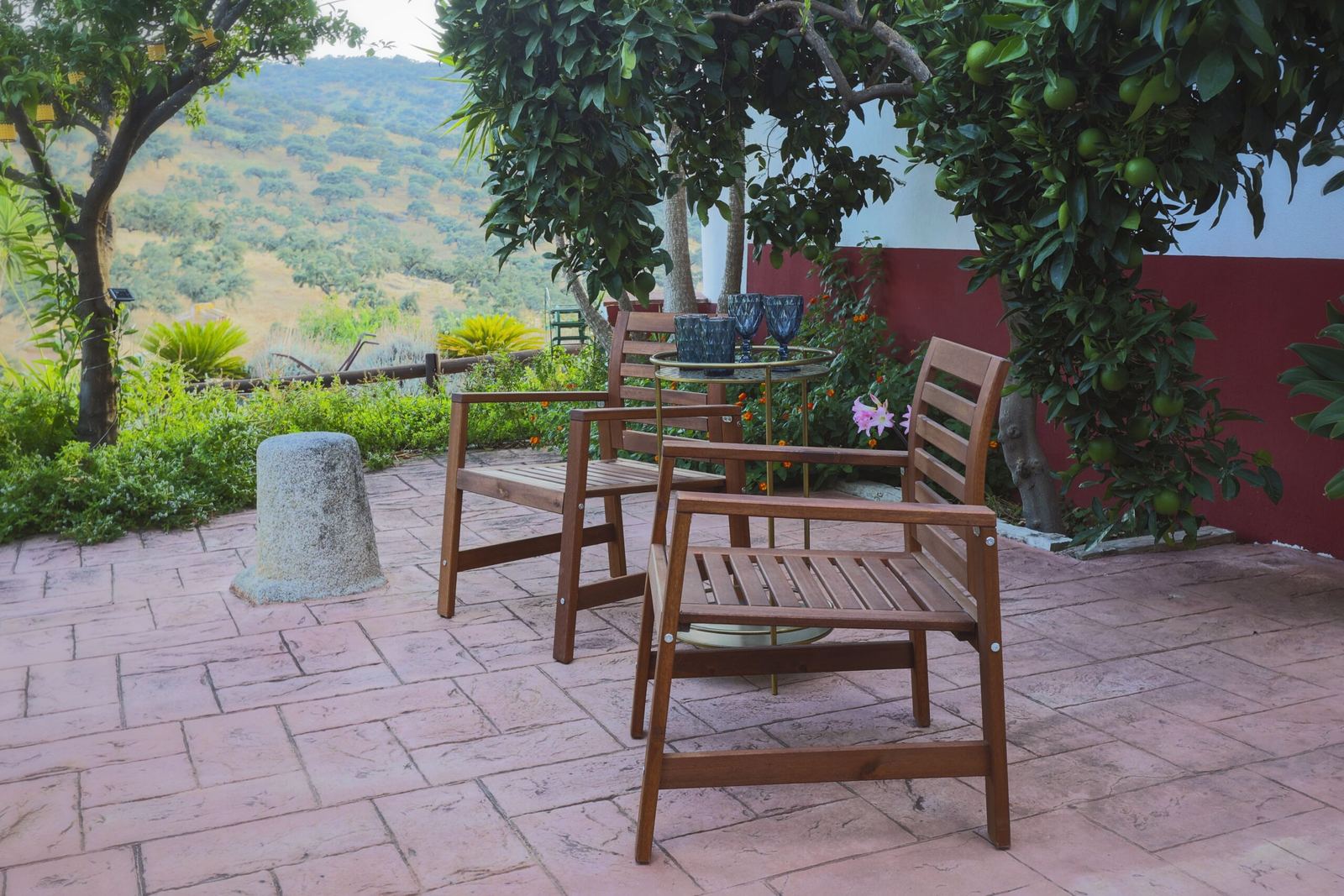 Terraza con dos sillones de madera bajo los naranjos, junto a la pared encalada con su zócalo de almagre; al fondo, la sierra