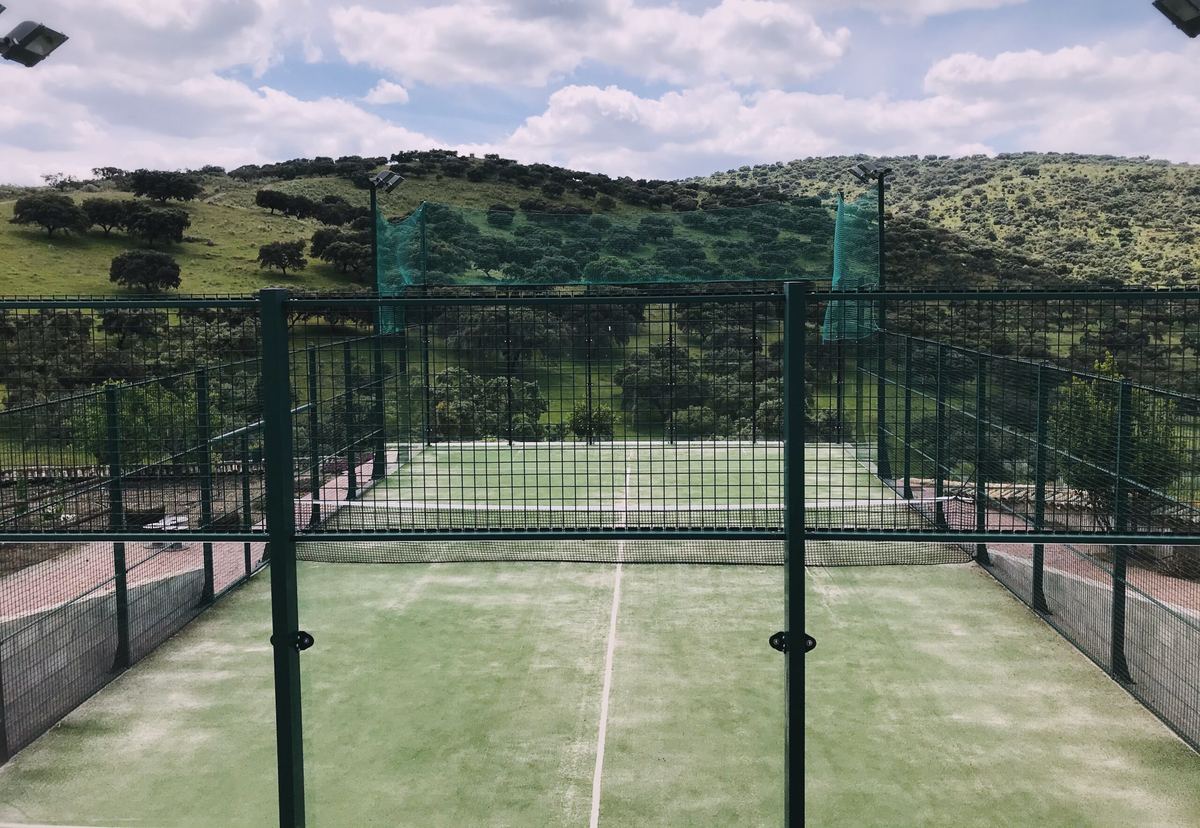 La pista de pádel con malla, y detrás las lomas de encinas
