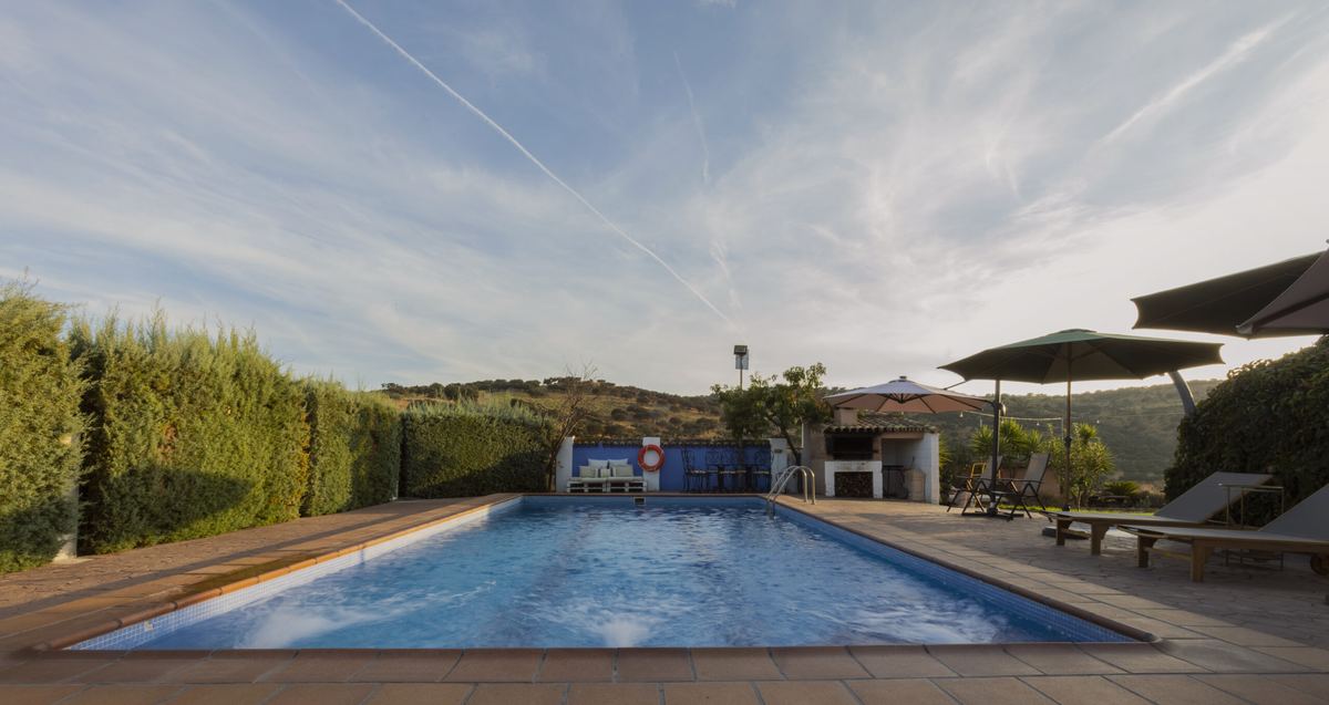 La piscina con tumbonas y sombrillas; detrás, el seto y la sierra