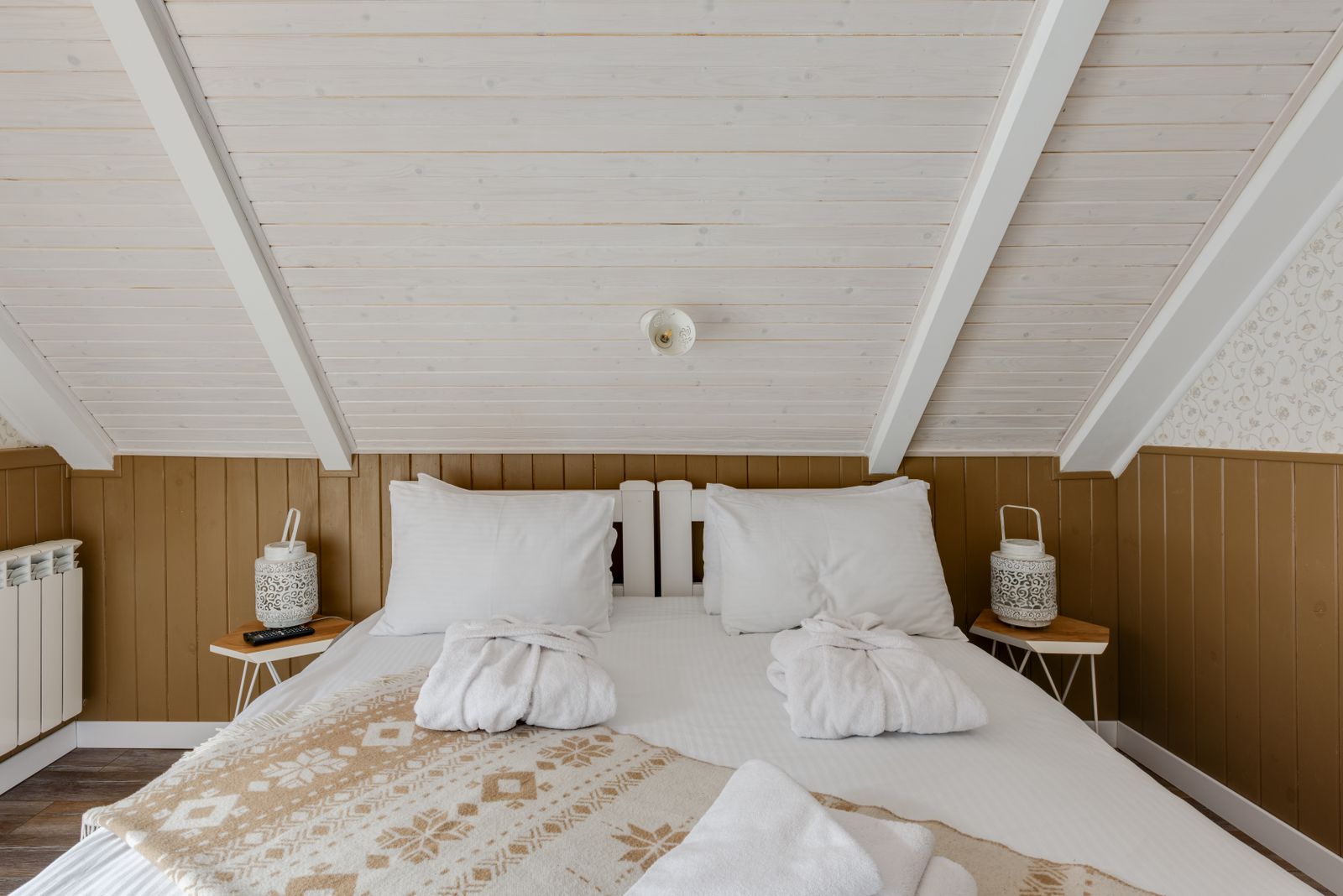 Buhardilla encalada con cama de madera, ropa blanca y albornoces doblados