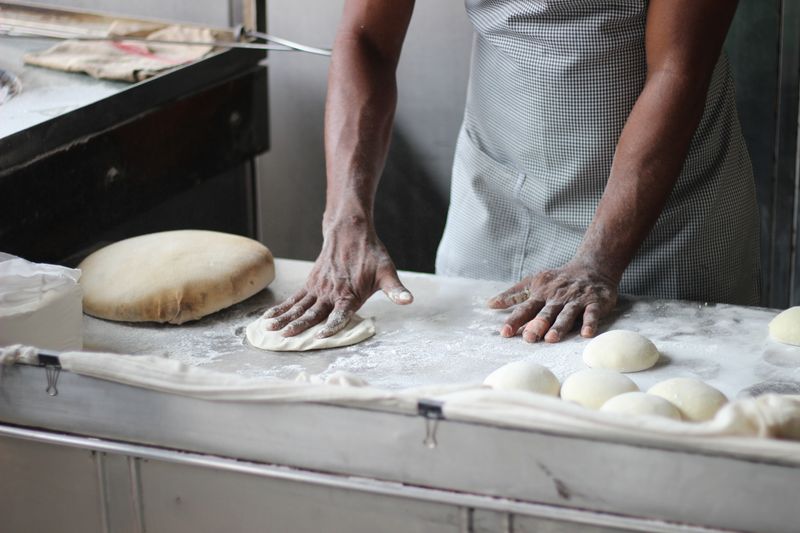 Manos de panadero trabajando una masa sobre la mesa enharinada.